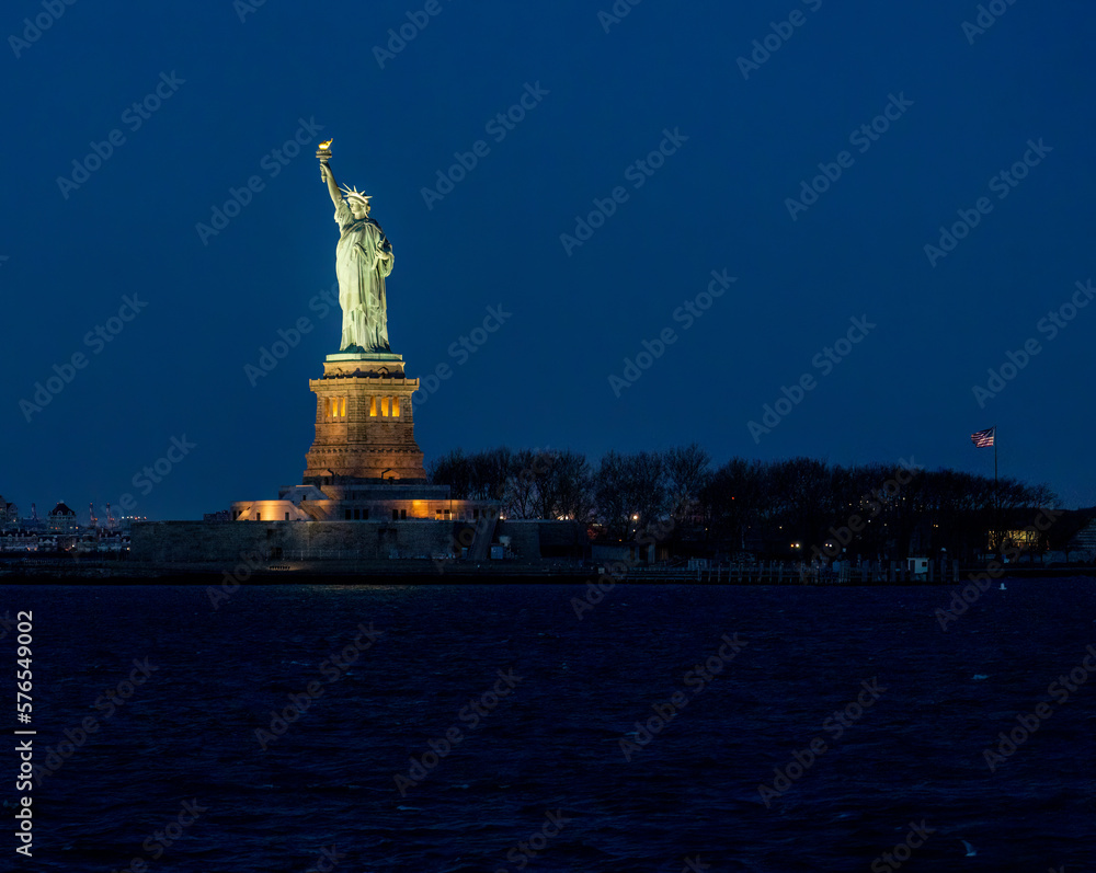 Night Profile of the Statue of Liberty from the Water with US flag in the background Night Profile of the Statue of Liberty from the Water with US flag in the background
