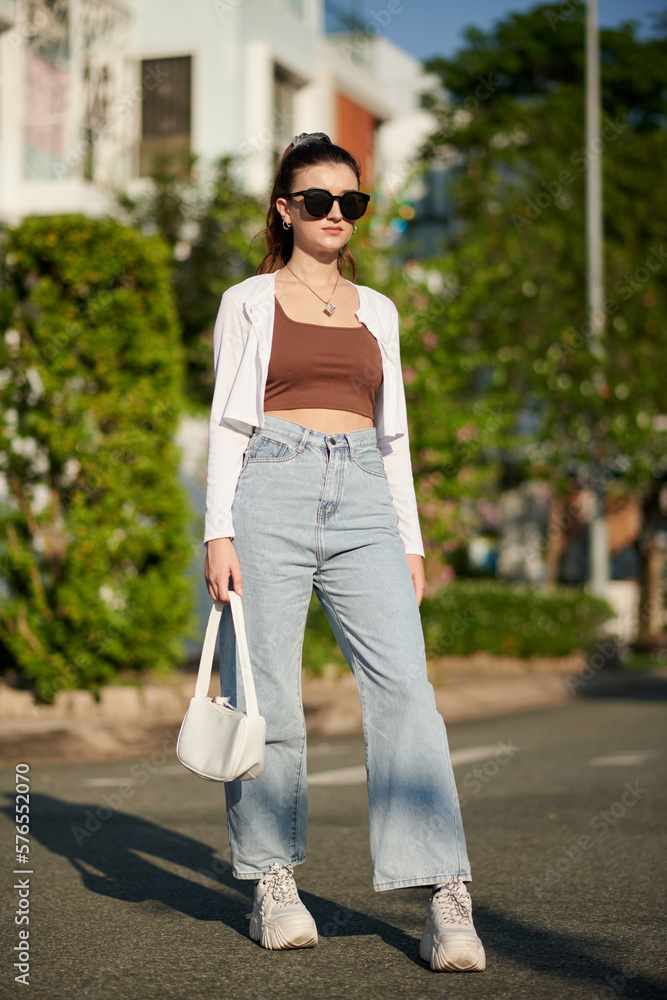 Fototapeta premium Young woman in wide jeans, sunglasses and white cardigan
