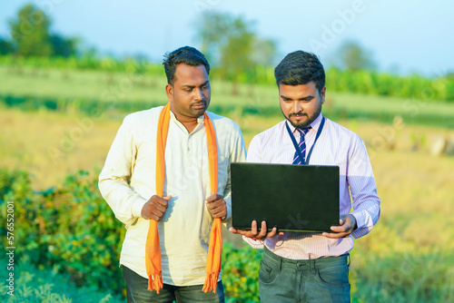Young Indian agronomist or banker showing some information to farmer in laptop 