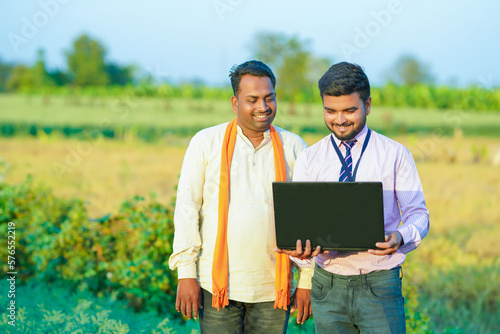 Young Indian agronomist or banker showing some information to farmer in laptop 
