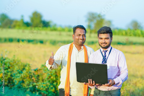 Young Indian agronomist or banker showing some information to farmer in laptop 