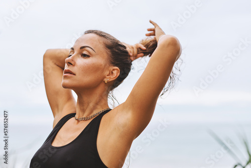 Beautiful girl taking break during yoga exercises, collecting curly dark hair in front of sea