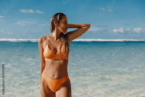 Portrait of tanned woman in yellow bikini at ocean beach.