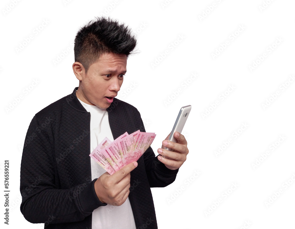 Handsome man with surprised facial expression looking at mobile screen and holding indonesian money Handsome man with surprised facial expression looking at mobile screen and holding indonesian money