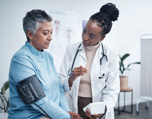 Black woman, doctor and senior patient with blood pressure reading for wellness, advice and conversation. Medic, elderly client and medical tools for health, cardiology and results in hospital office photo
