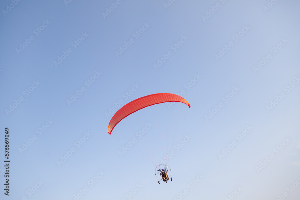 a red motorized paraglider in the blue sky flies with two passengers on a warm summer day. Flying sports. a red motorized paraglider in the blue sky flies with two passengers on a warm summer day. Flying sports.