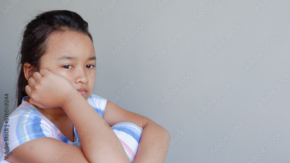 pensive little asian girl with pigtails over gray background.