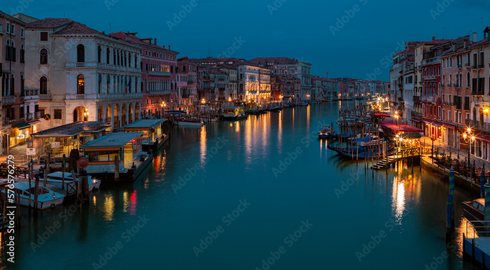 A canal in venice at night with lights on the buildings and boats on the water.