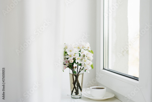 Spring flowers in a vase and a cup of tea or coffee in a white porcelain mug on the windowsill