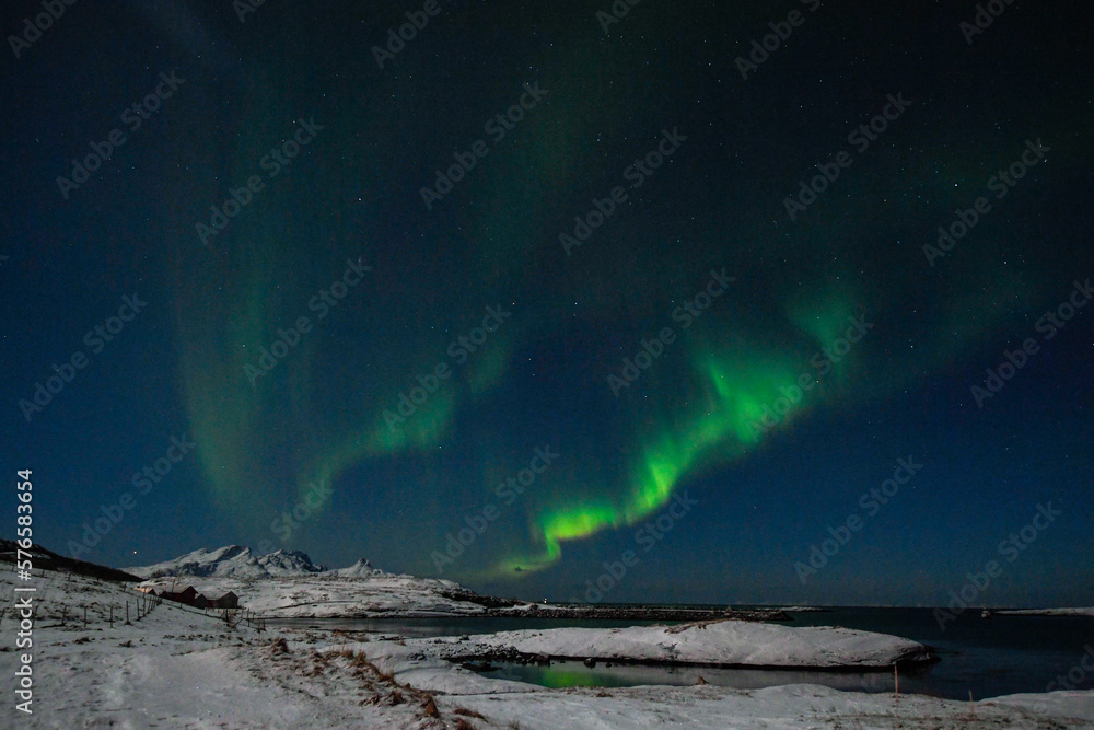 Bright Green Colours of the Northern Light, Aurora Borealis illuminate the Night Sky over the beach at Mjelle, in Arctic Norway.