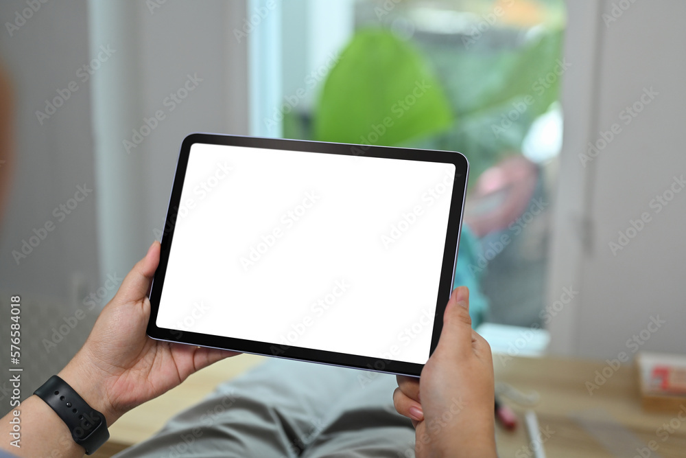 Close up view of hands holding holding digital tablet while sitting in living room. White screen for webpage or advertise text Close up view of hands holding holding digital tablet while sitting in living room. White screen for webpage or advertise text