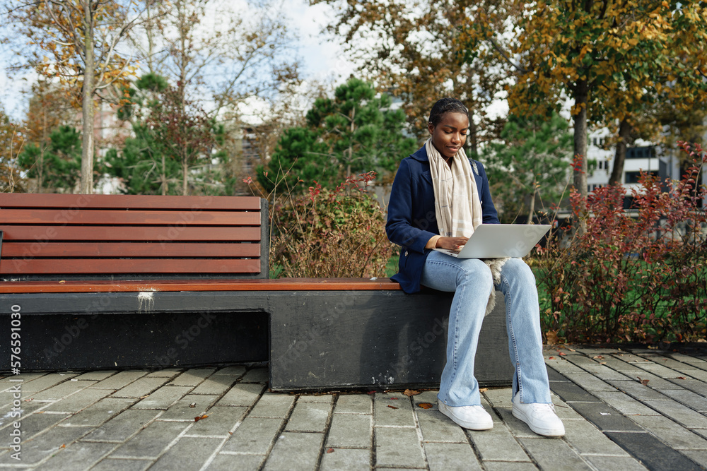 Young african businesswoman using laptop while sitting on the bench in the city Young african businesswoman using laptop while sitting on the bench in the city