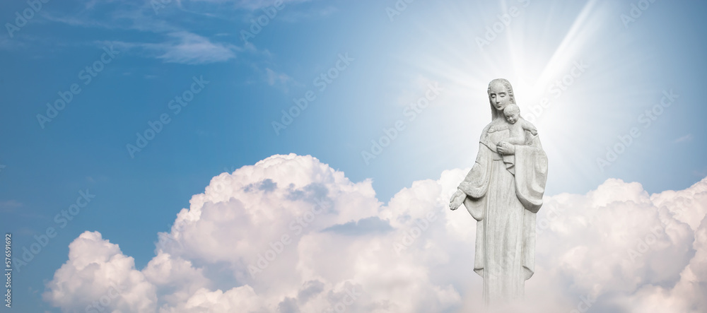 Fototapeta premium Mother Mary and Baby Jesus Statue against blue sky with white clouds background.