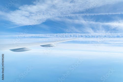 Wing of an airplane jet flying above clouds with blue sky from the window in traveling and transportation concept. Nature landscape background. © tampatra
