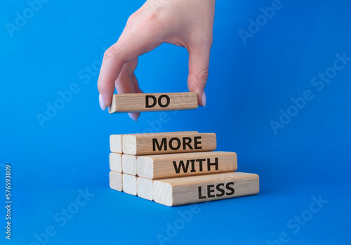Do more with less symbol. Concept words Do more with less on wooden blocks. Businessman hand. Beautiful blue background. Businessman hand. Business and Do more with less concept. Copy space. photo