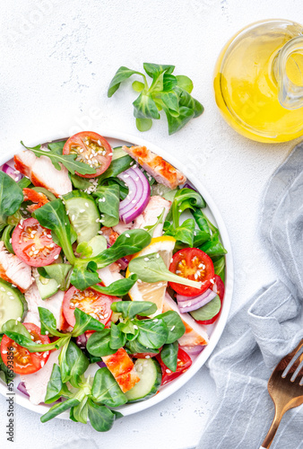 Fresh salad with grilled chicken slice with red tomato, cucumber, red onion, lamb lettuce and sesame seeds on white table background, top view