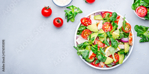 Chicken salad with red tomato, avocado, cucumber, red onion, lamb lettuce and sesame seeds on gray table background, top view banner