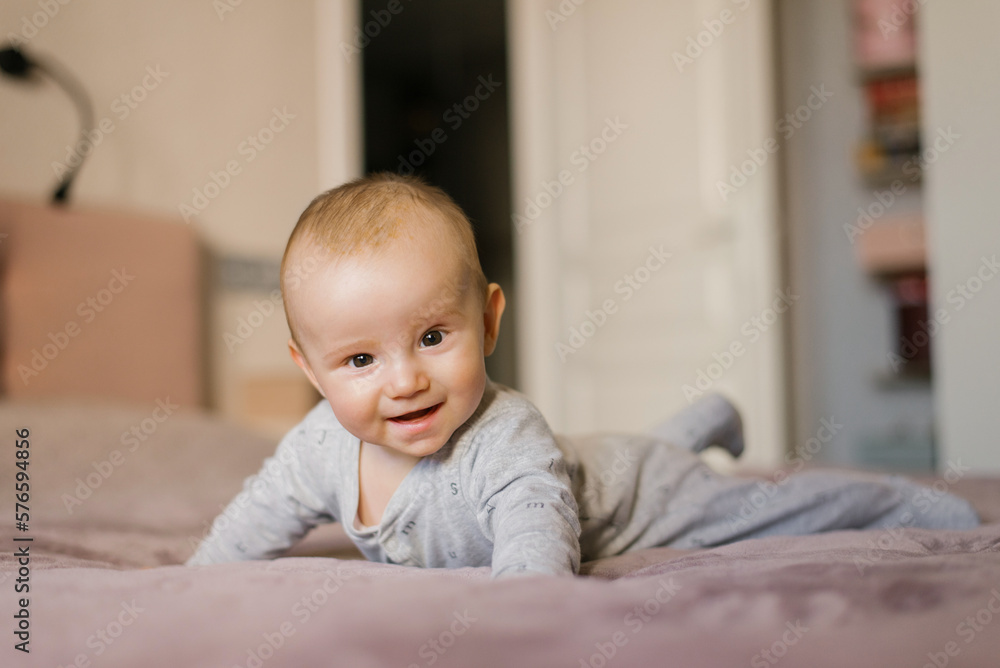 Cute baby is lying on his stomach holding on his elbows on the bed Cute baby is lying on his stomach holding on his elbows on the bed