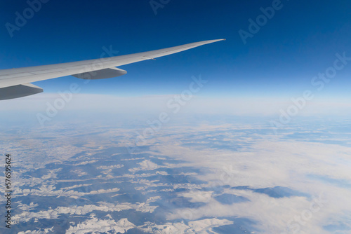 Wing of an airplane jet flying above clouds with blue sky from the window in traveling and transportation concept. Nature landscape background.