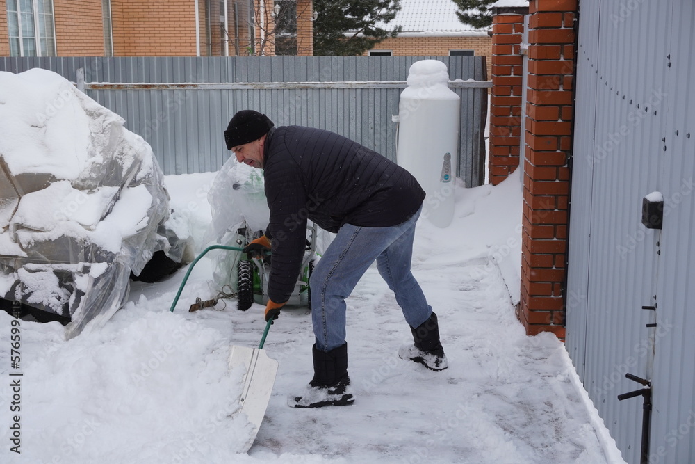 A man cleans snow in the winter in the courtyard of the house. A man cleans snow in the winter in the courtyard of the house.