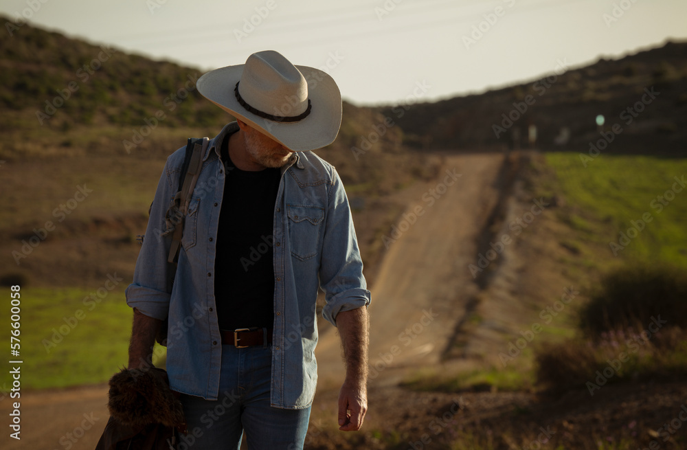 Adult man in cowboy hat on dirt road against sky