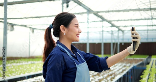 Asian young woman taking live chat with a cellphone in vegetables hydroponic farm. Asian farmer video calls online selling harvest of organic vegetables in hydroponic system farm