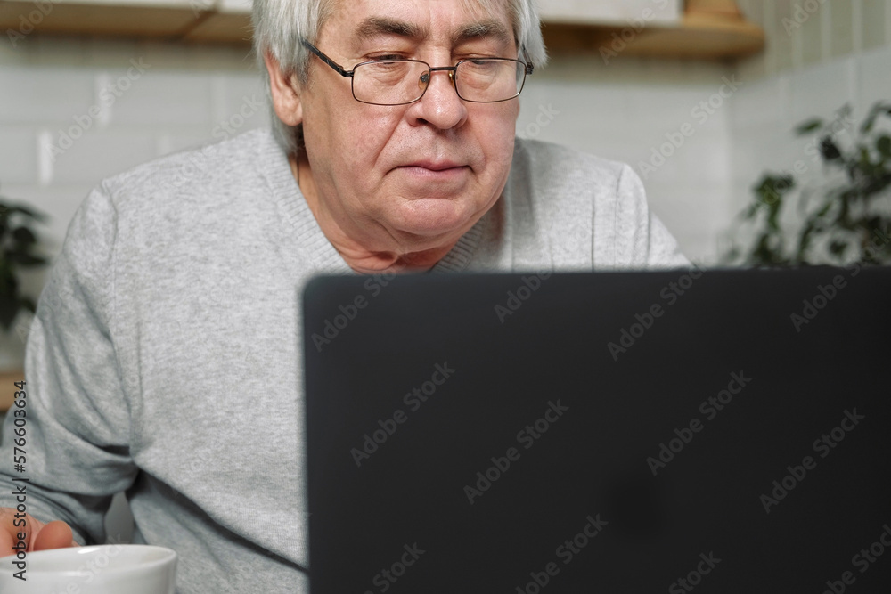 Senior male business owner in glasses sitting at desk in front of laptop. Successful older male working at home. Grey haired 60s - 70s Aged busy man typing keyboard looking at display. Distance office Senior male business owner in glasses sitting at desk in front of laptop. Successful older male working at home. Grey haired 60s - 70s Aged busy man typing keyboard looking at display. Distance office