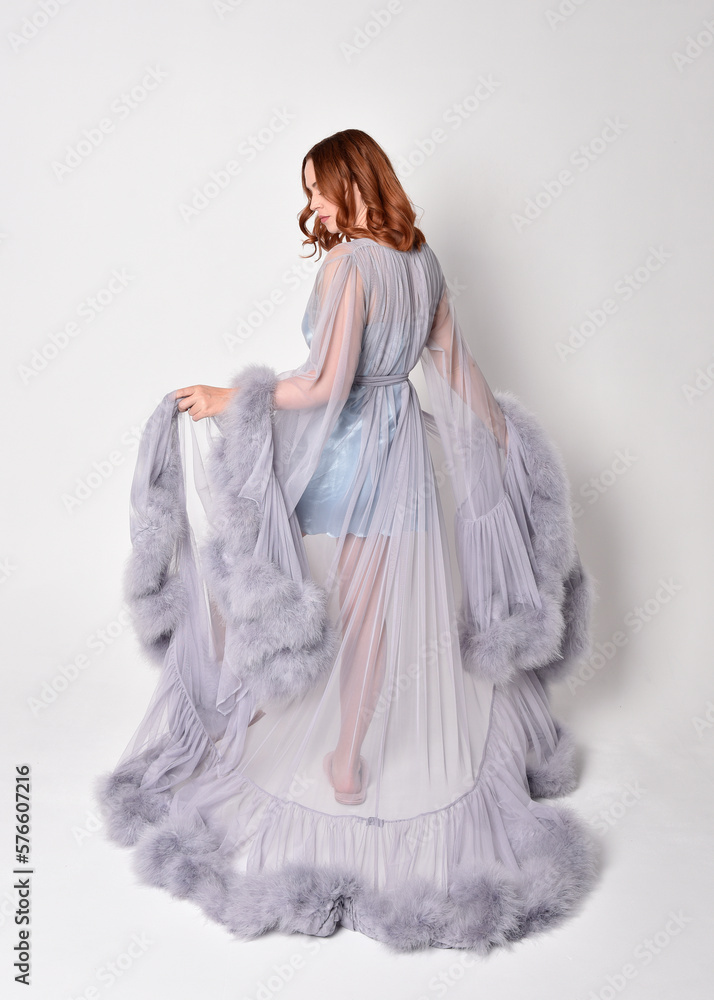 Portrait of beautiful red haired woman wearing glamorous  fluffy bridal dressing gown and vintage pearl necklace.  Elegantly standing pose, isolated on white studio background.