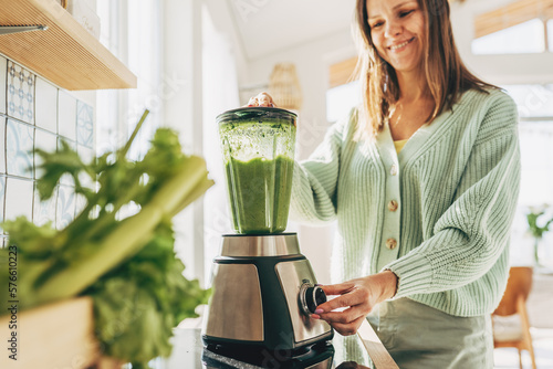 Woman preparing tasty green smoothie in kitchen