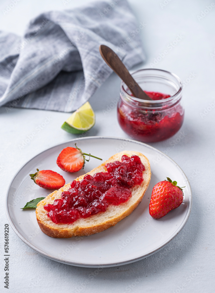 Strawberry jam on a piece of bread on a plate on a blue background with fresh berries and jar with jam. Strawberry jam on a piece of bread on a plate on a blue background with fresh berries and jar with jam.