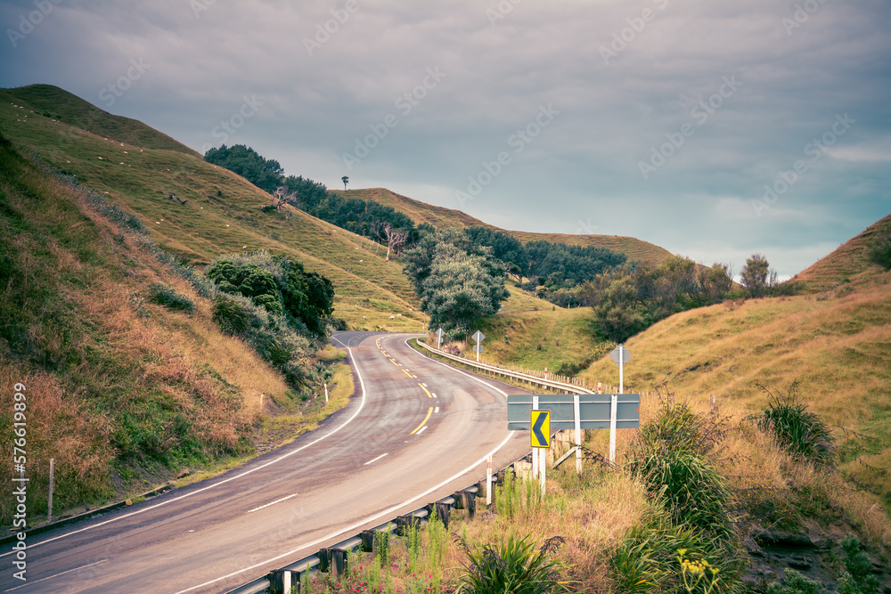 Retro style photo of a narrow monutain road winding through green hills. Pacific Coast Highway, Gisborne, North Island, New Zealand. Toned image