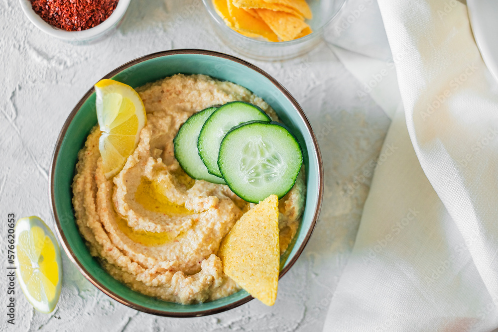 Hummus in a bowl, decorated with boiled chickpeas, olive oil, lemon, cucumber and crisps on a light background. Top View.