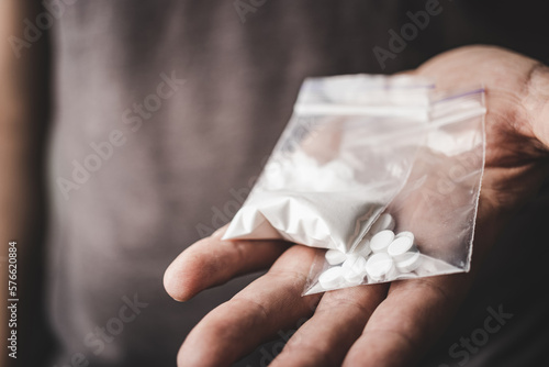 Foto Man's hand holds two transparent plastic packets with cocaine powder and white pills lsd, drug dealer selling drugs