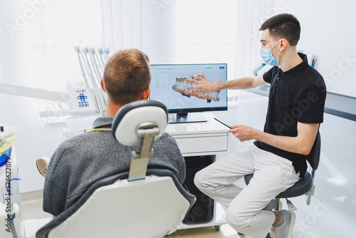 A young dentist doctor tells a male patient about dental care. A man was sitting in a dental chair at a doctor s appointment. Modern dental treatment