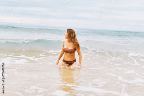 Young adorable woman is standing and relaxing on the sand beach at the wind