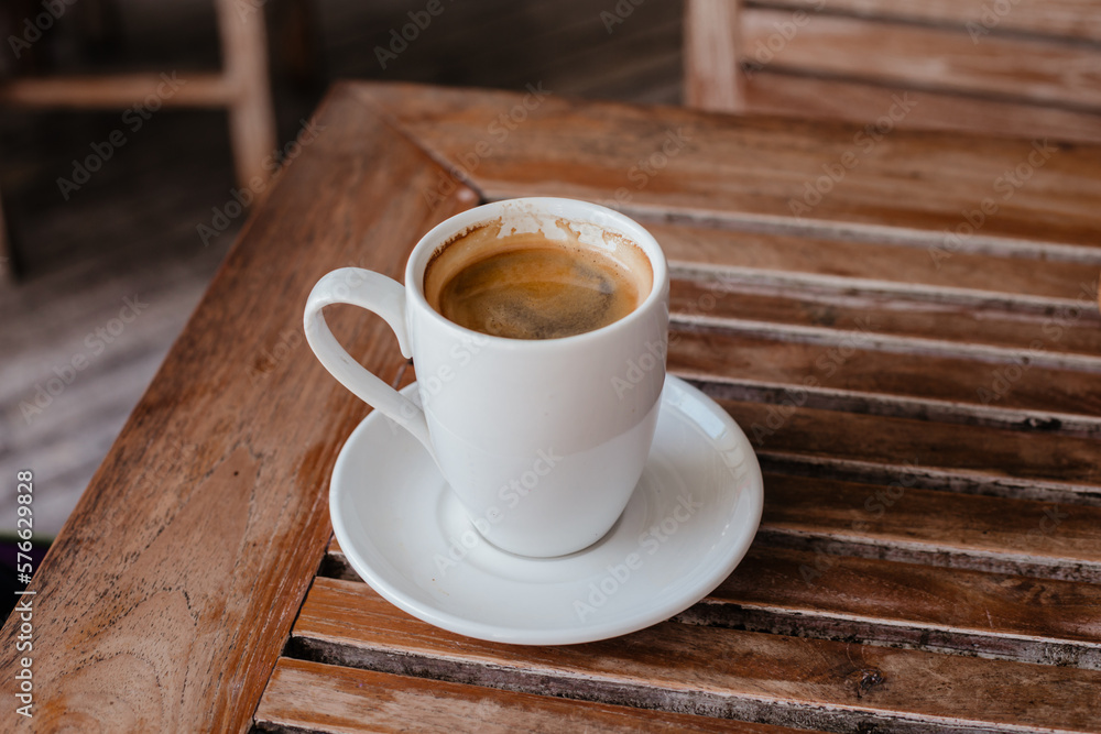 Fototapeta premium Black coffee in a large white mug on a wooden table. Hot double americano on the veranda with space for text