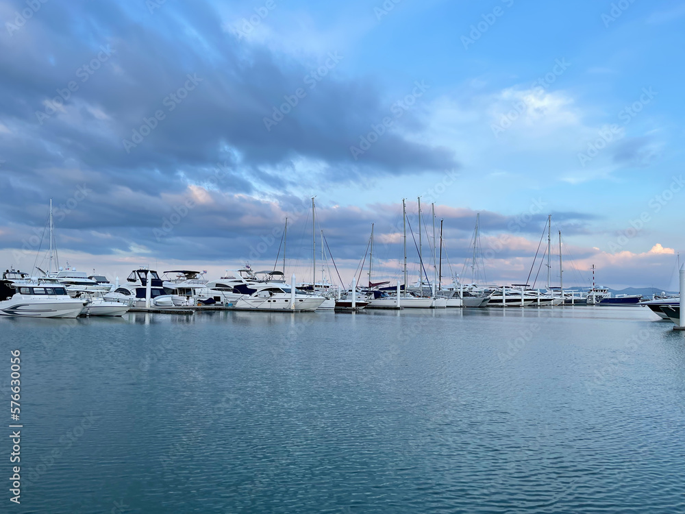 Yachts in marina. Luxury sailing yachts line up on the horizon in a calm tropical bay. Amazing pink sunset. Sapphire sky, blue sea, colorful clouds. Sea navigation and sailing season. Sailboats