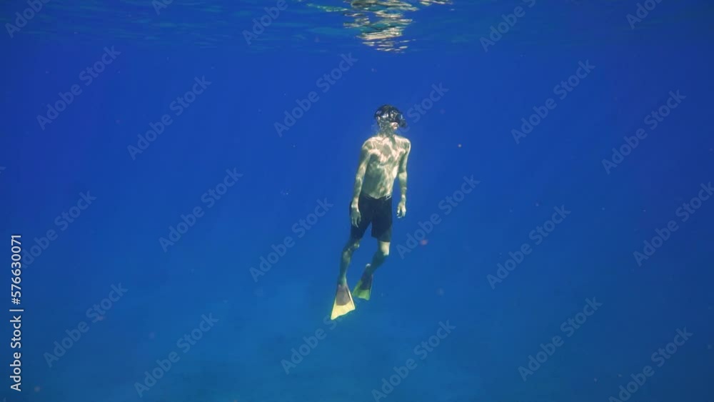 Man rises from depths of the ocean, light rays shimmer through water Man rises from depths of the ocean, light rays shimmer through water