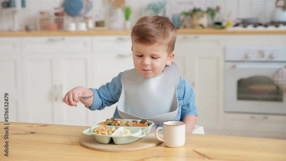 Adorable caucasian toddler boy eats vegetables on his own, pricking them on fork. The concept of self-feeding. BLW. Child eats healthy vegetables with meat on a high chair. Mock up. Place for text Adorable caucasian toddler boy eats vegetables on his own, pricking them on fork. The concept of self-feeding. BLW. Child eats healthy vegetables with meat on a high chair. Mock up. Place for text