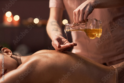 Hands of masseuse applying natural oil on back of female client