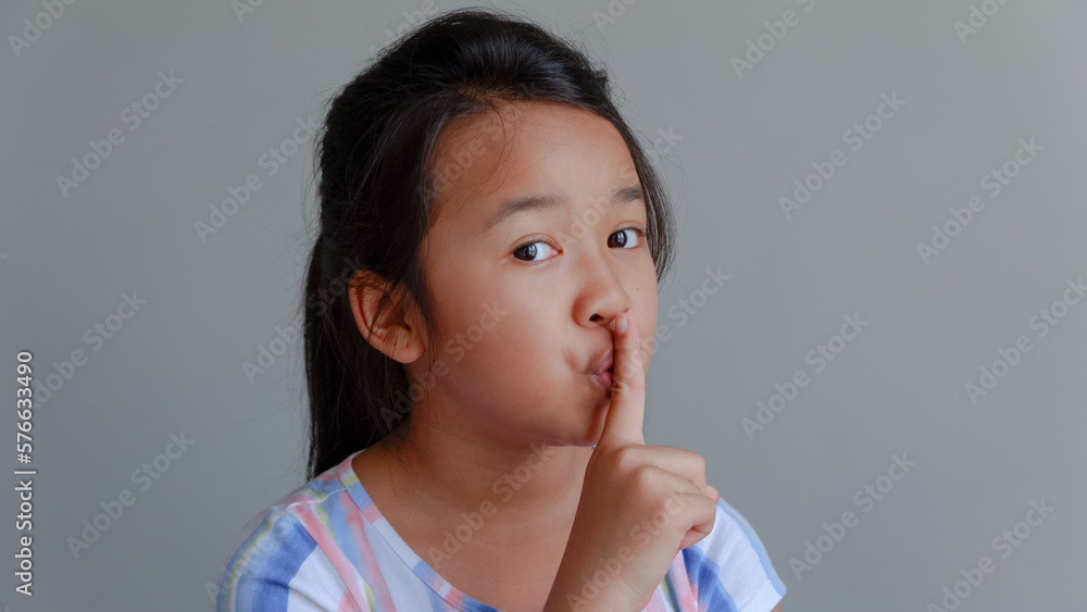 Calm beautiful asian girl looking camera and making silence gesture isolated over gray Calm beautiful asian girl looking camera and making silence gesture isolated over gray