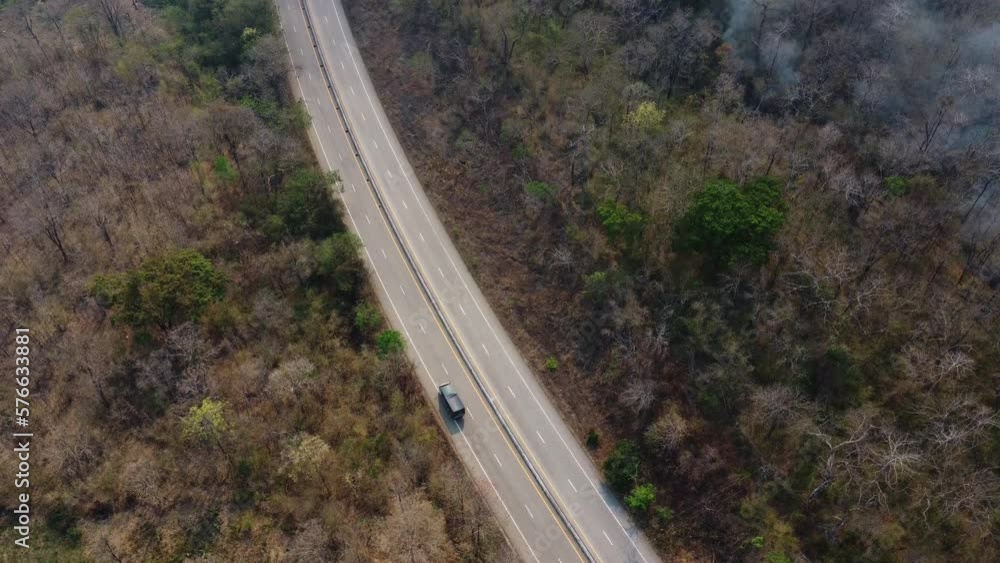 Aerial drone view of a wildfire burning through a forest area, fills the sky with dark smoke in the woods near the edge of the highway. Burning Forest. Air pollution concept Aerial drone view of a wildfire burning through a forest area, fills the sky with dark smoke in the woods near the edge of the highway. Burning Forest. Air pollution concept