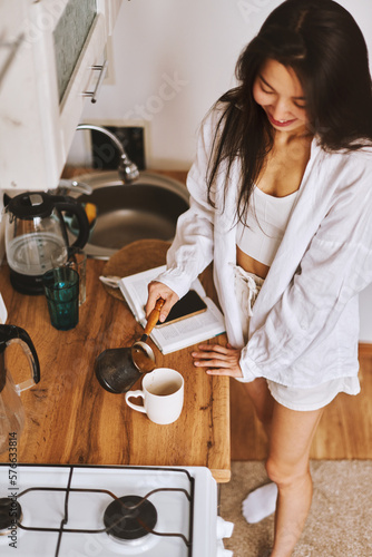Portrait long hair brunette Asian woman in white clothes making morning hot cup coffee in kitchen