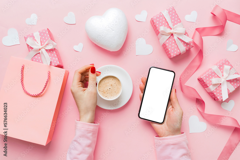 Female hands holding smart phone with coffee for Valentine day, gift box and envelope, hearts Female hands holding smart phone with coffee for Valentine day, gift box and envelope, hearts