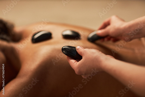 Spa therapist putting hot stones on back of young woman