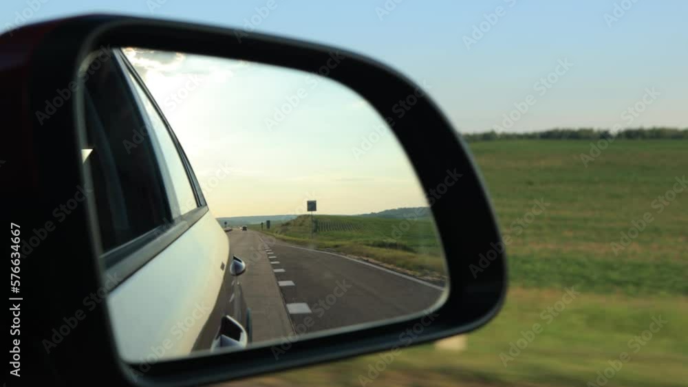 View in the rear view side mirror of a automobile, driving a red car along the road