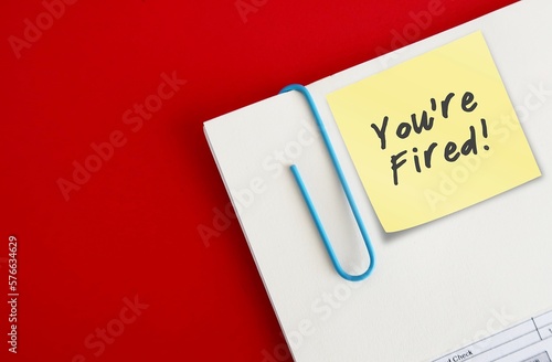 Document from boss with note written YOU'RE FIRED on copy space red background, concept of full time employee getting fired or employer make decision to let go low performance corporate worker photo