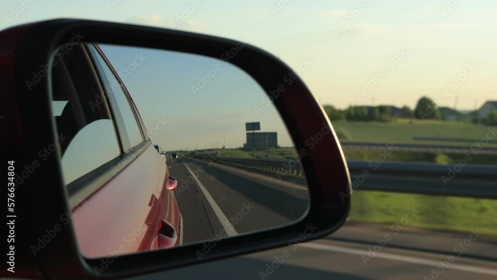 View in the rear view side mirror of a automobile, driving a red car along the road View in the rear view side mirror of a automobile, driving a red car along the road