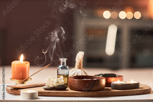 Burning incense stick, candles and bowl of salt scrub on table in spa salon