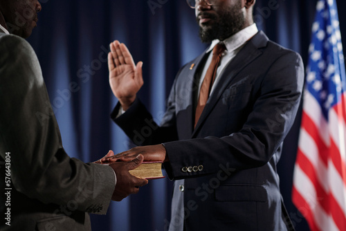 Close-up of young African American man in formalwear giving oath of office with one hand open and the other one on Holy Bible photo
